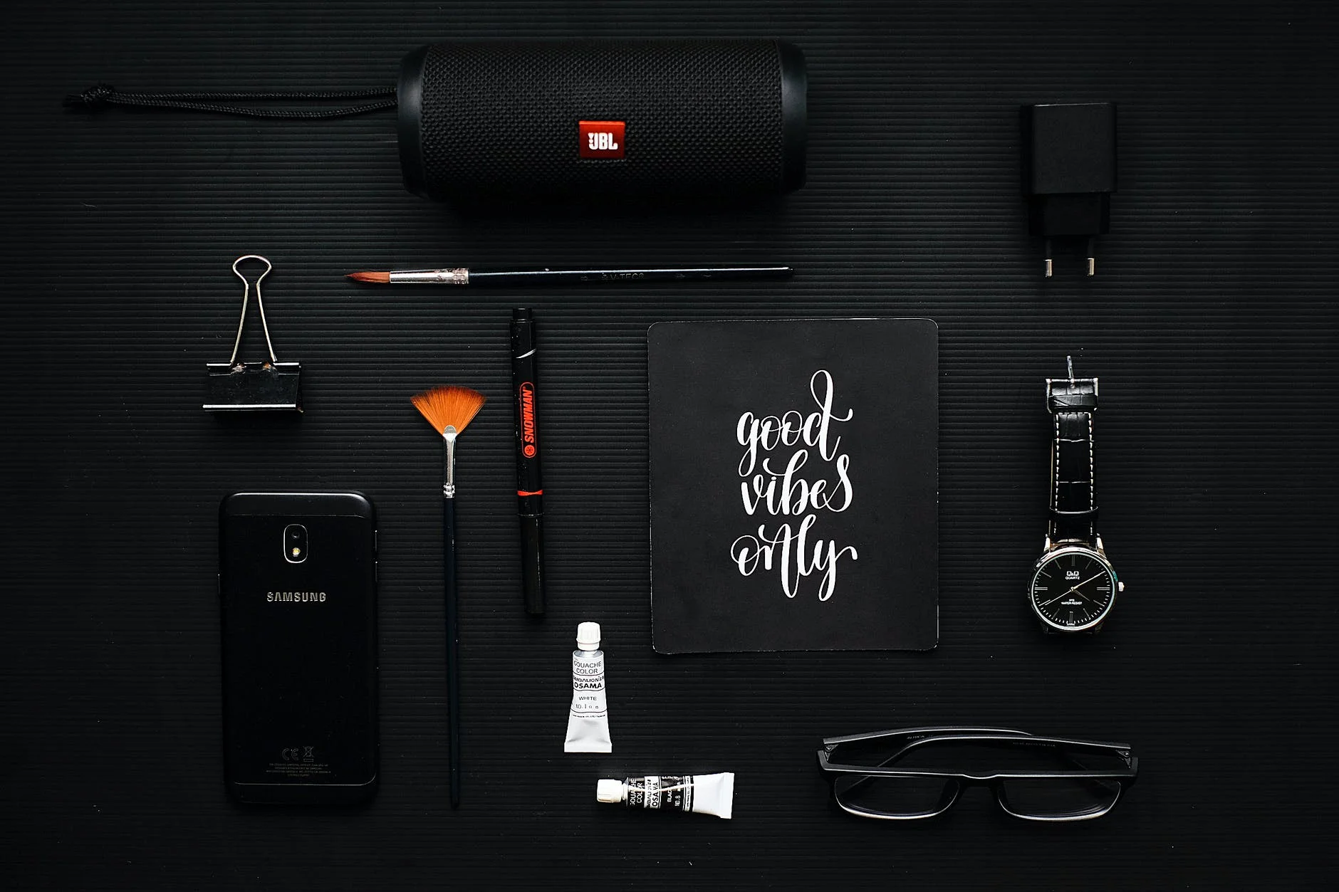 close up photography of smartphone beside binder clip speaker and eyeglasses on black textile